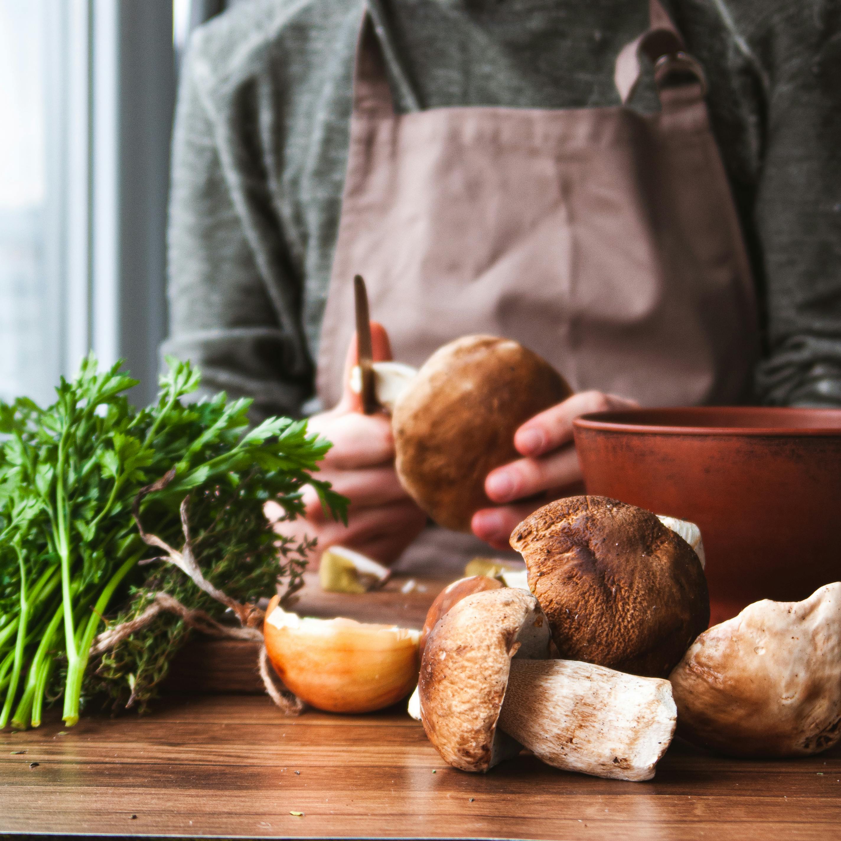 Close-up of a chef in an apron preparing mushrooms and parsley in a kitchen setting.