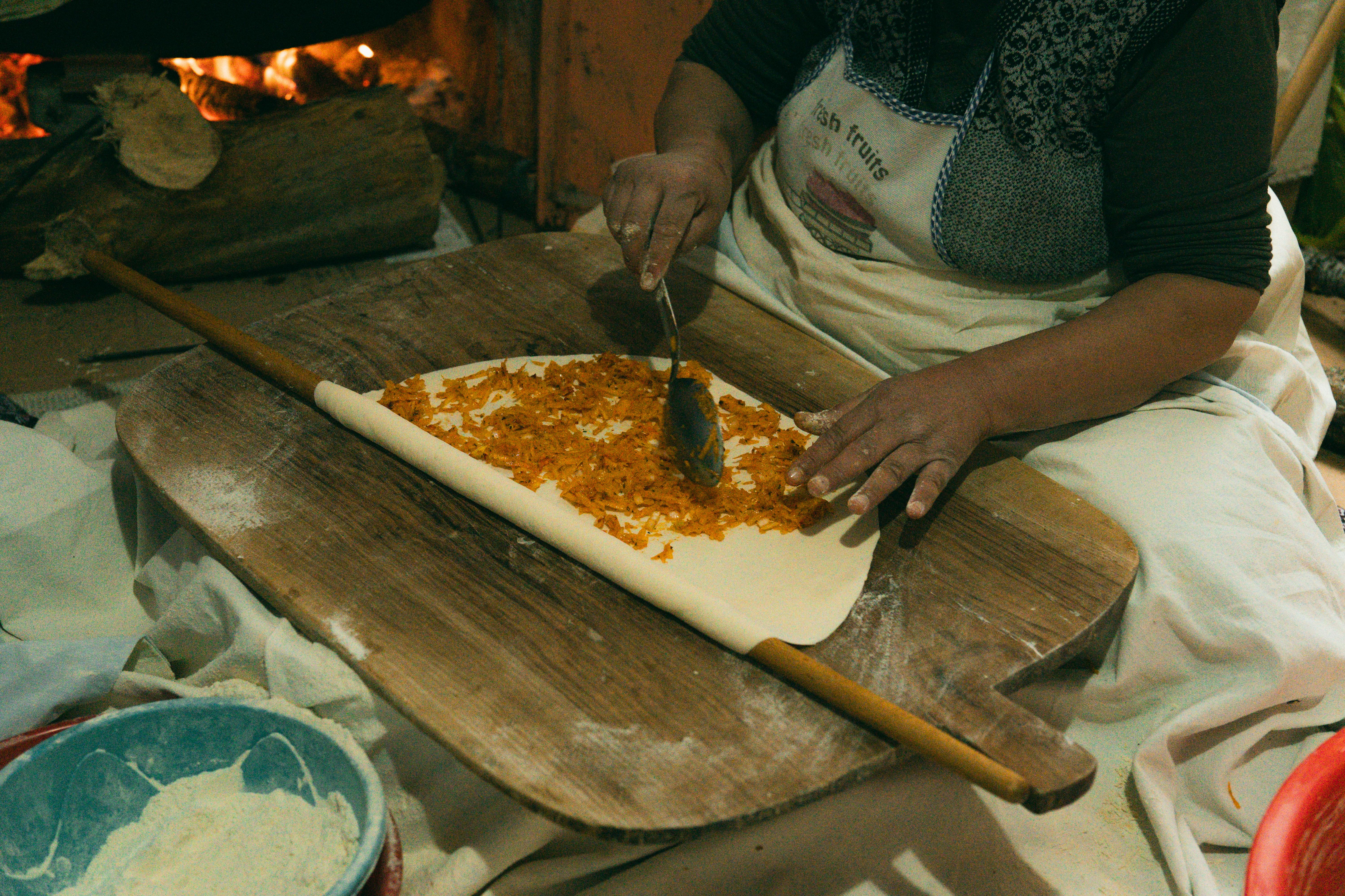 Woman prepares traditional Turkish borek with filling on dough indoors.